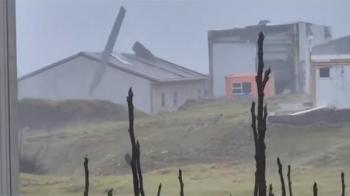 Stills grabbed from Fouche Condries video (right),
show roofing debris flying through the air (above)
and a building stripped of cladding by the wind (below).
Big Point is just visible in the background.
