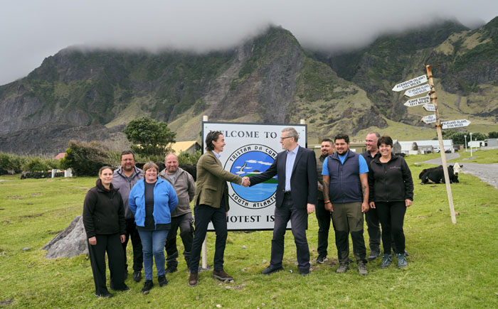 Tristan Administrator Philip Kendall shaking hands with James Wallace with Island Council members by the famous Tristan sign