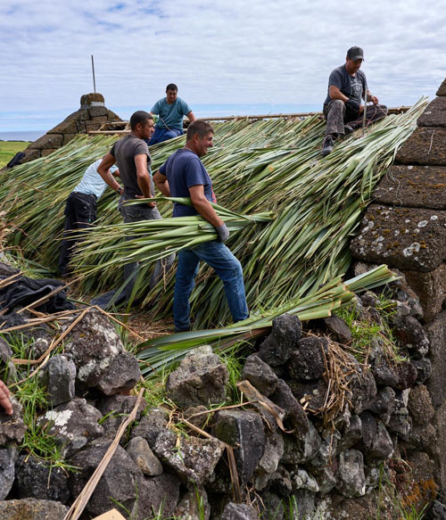Men at work laying flax bundles on the roof.