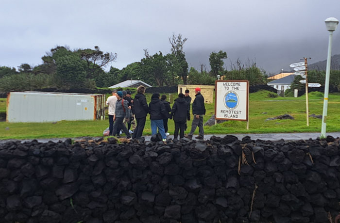 Visitors gather for a walking tour at the 'Remotest Island' sign